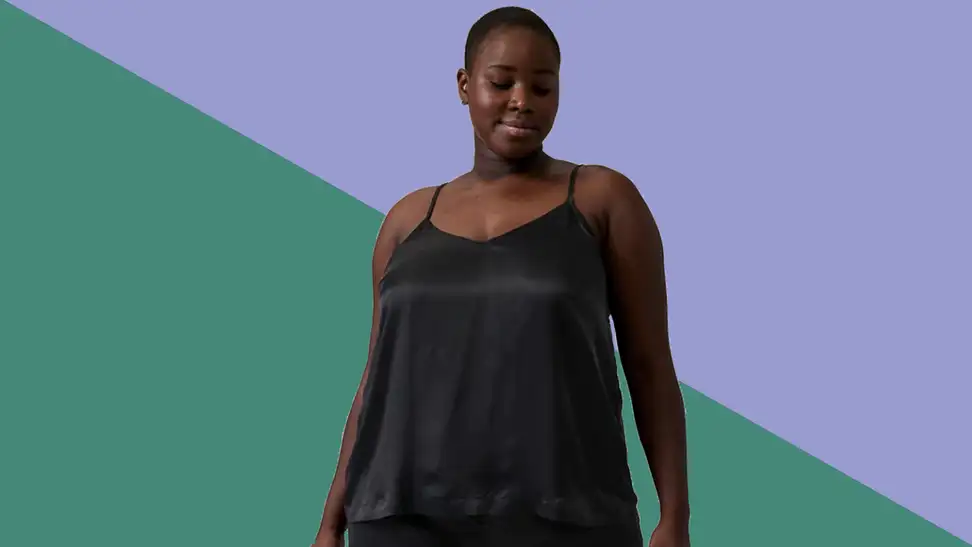 An image of a woman in a black silky cami top on a green and purple background.