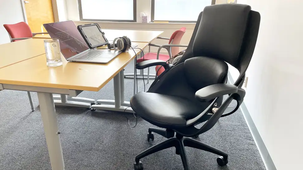 A downward view of the chair sitting at one of the conference room tables in our office. There's a laptop and iPad set up in front of it with headphones attached.