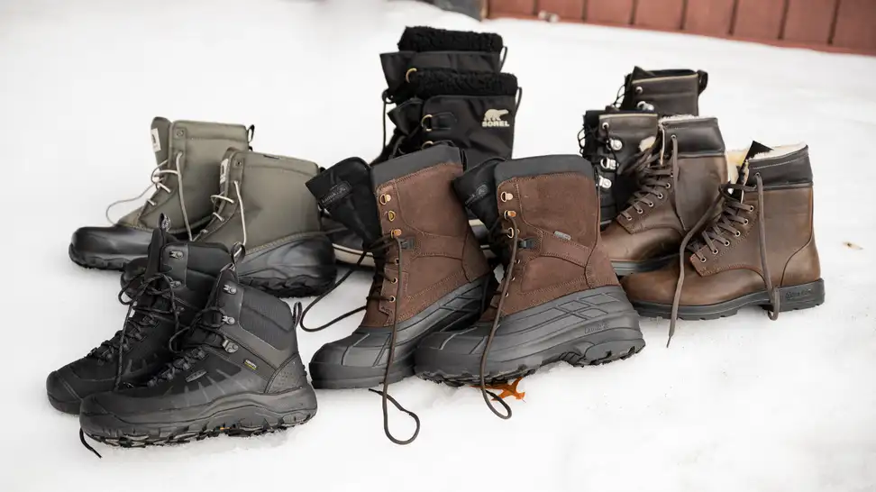 A wide selection of men's winter boots, sitting on a bank of snow.
