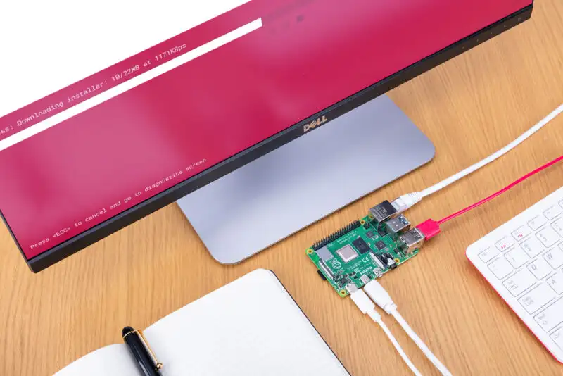Image of a small circuit board next to a keyboard, monitor, and notebook with a pen