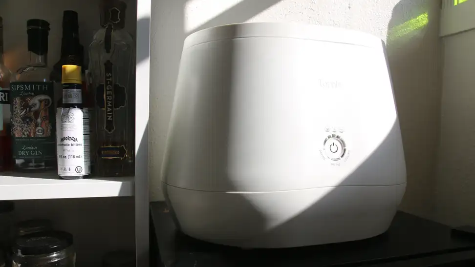 A Lomi composter sitting on a wine fridge near a cocktail shelf.