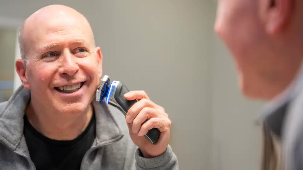A man looks in his bathroom mirror as he shaves his face.