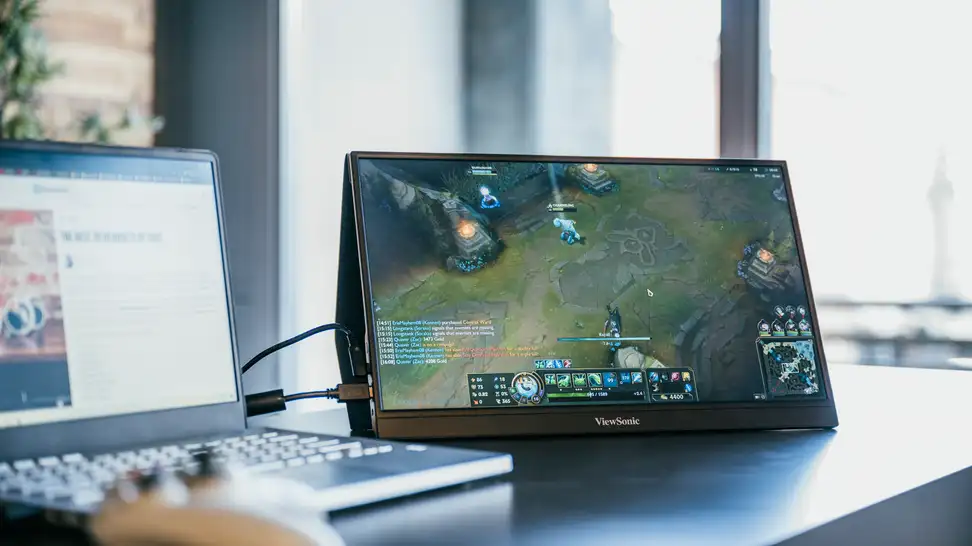 A small, portable gaming monitor standing upright on a desk with a controller attached