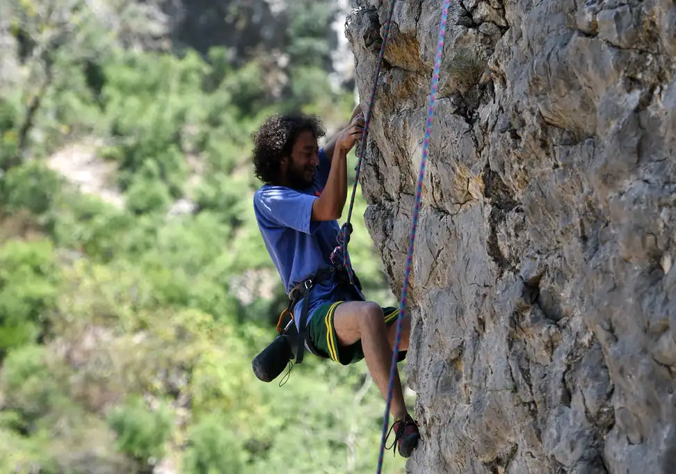 A person climbing a rock wall with climbing shoes and a harness.