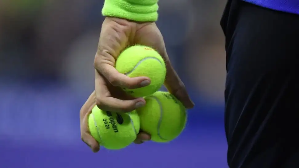 A hand grasps three lime-green tennis balls.