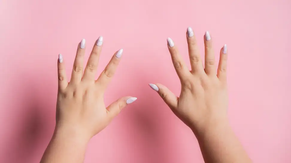 Two hands with press-on nails on them held up in front of a pink wall.