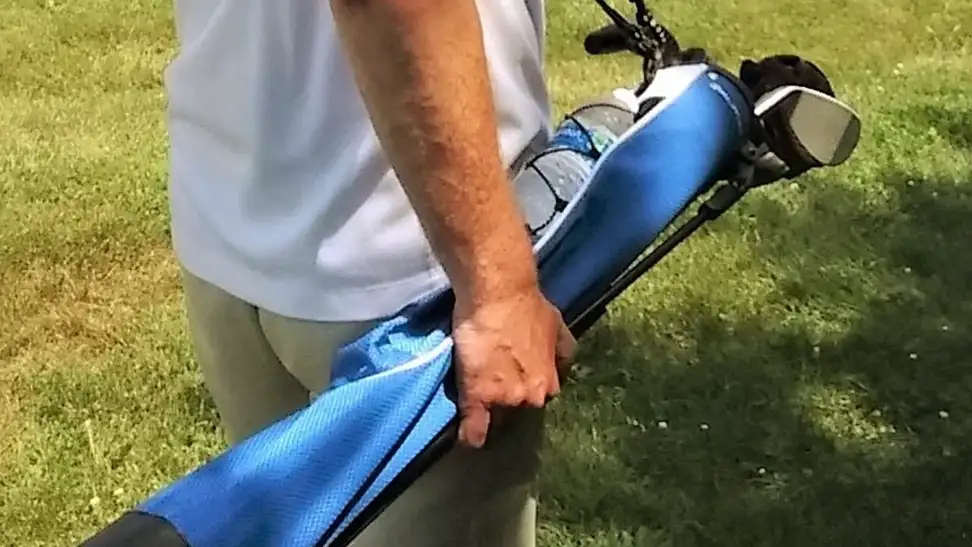 A guy carrying his golf bag to the golf course for a tournament.