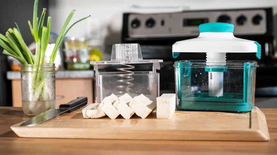 TofuXpress and Noya Tofu Press on a wooden cutting board with sliced tofu in front, on a kitchen countertop.