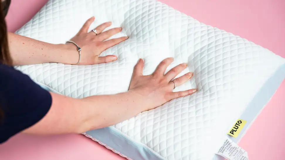 A pair of hands pushing down a Pluto Pillow.
