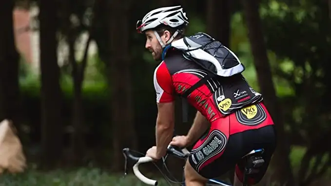 A guy riding his bike while wearing his camelback to stay hydrated.