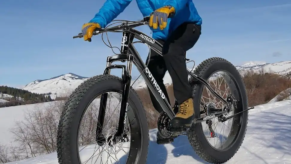 A guy riding his fat bike through snow.