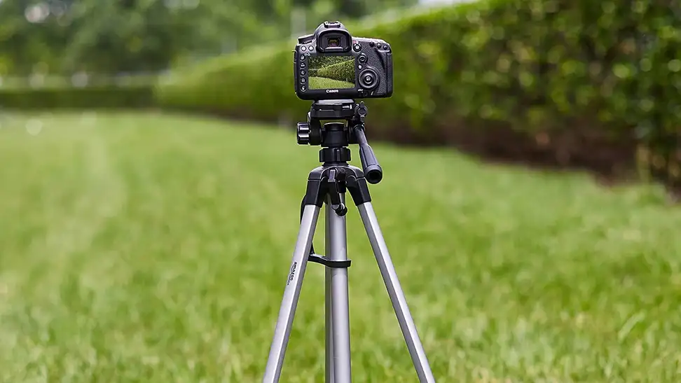 A tripod being used in a grass area to hold an iPhone that is taking photos.