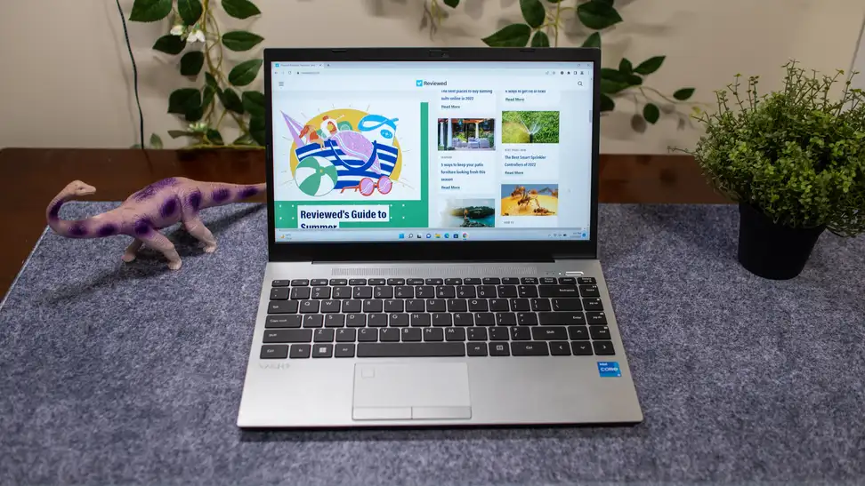 The laptop is open on a table with a plastic dinosaur and a plant.