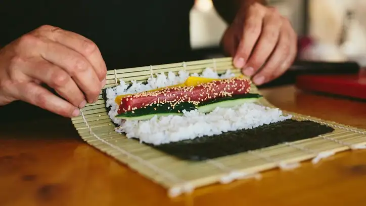 person using sushi mat to roll sushi