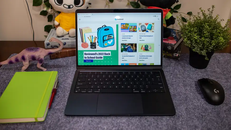 The MacBook Air laptop is on a table with a dinosaur, Glitch the cat, Gamer cat, a notebook, and a mouse.