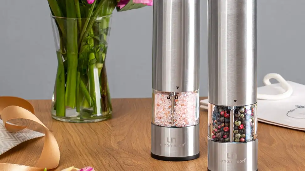 A set of salt and pepper grinders, sleek stainless steel, sit upright on a wooden table