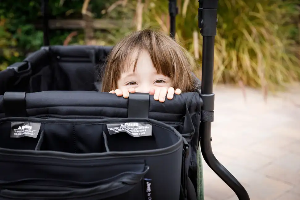 A child peeks over the top of a stroller wagon.