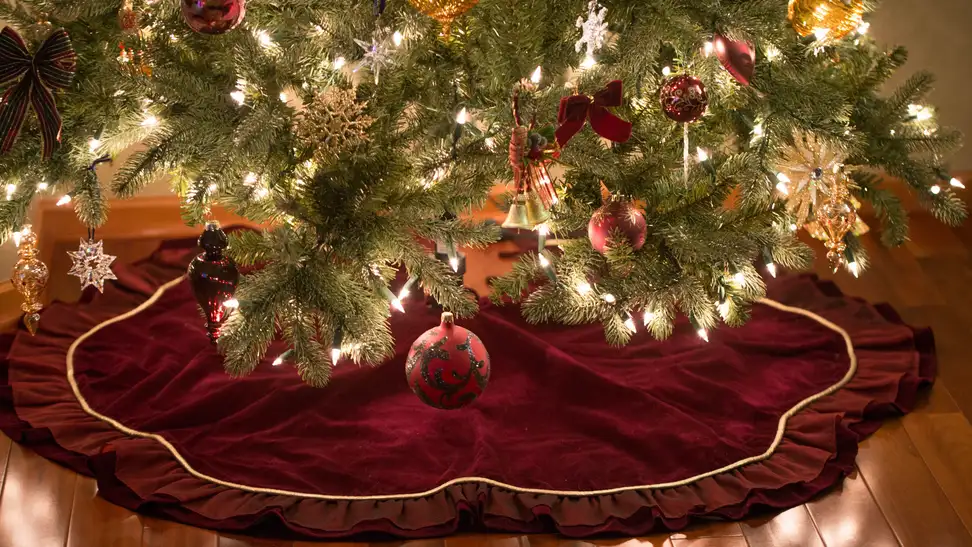 Dark red Christmas tree skirt with gold accent under lit Christmas tree