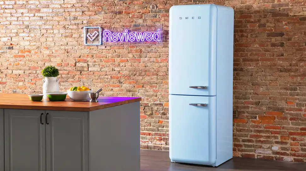 A tall blue Smeg column refrigerator stands in front of a brick wall