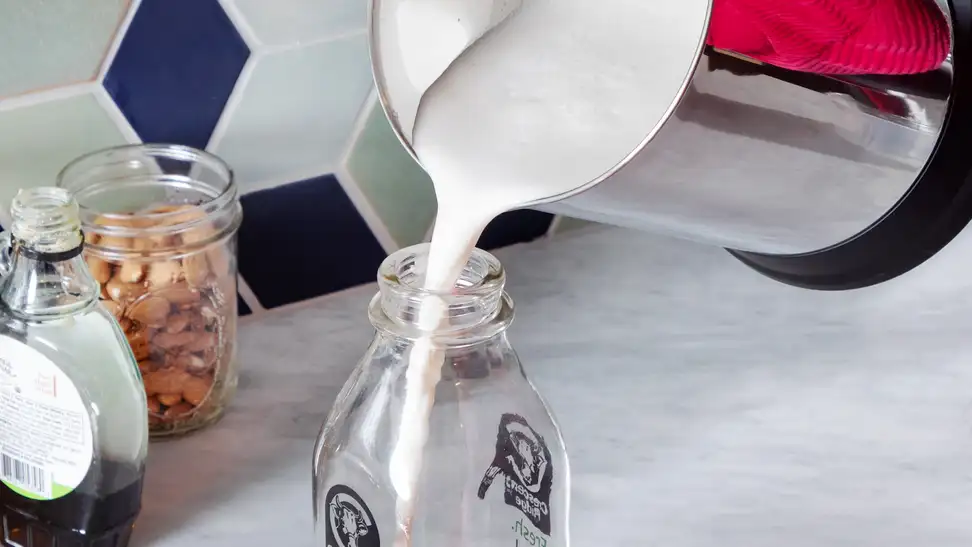 Person pouring plant-based milk from the Almond Cow plant-based milk maker into glass bottle.