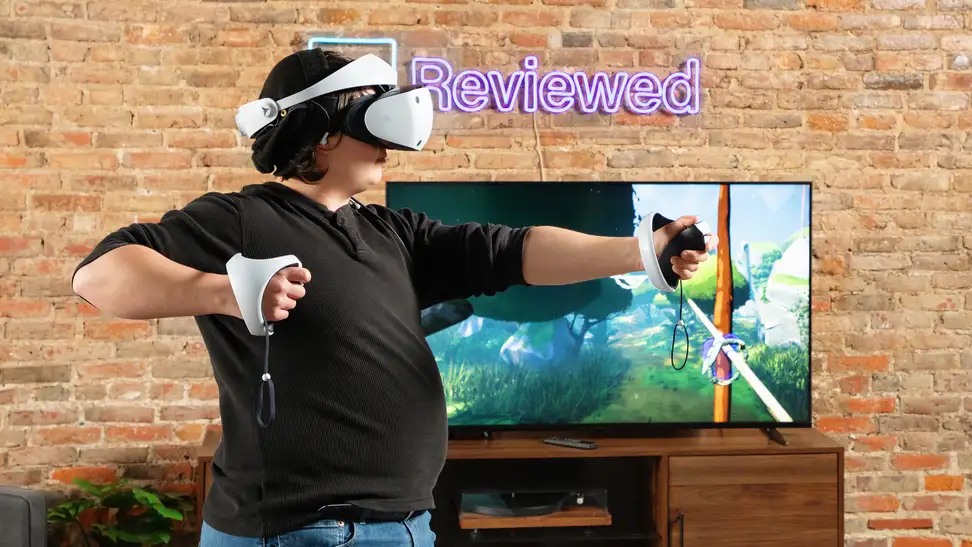 A person wearing a white PSVR 2 headset mimicking pulling back a bow and arrow in front of a TV