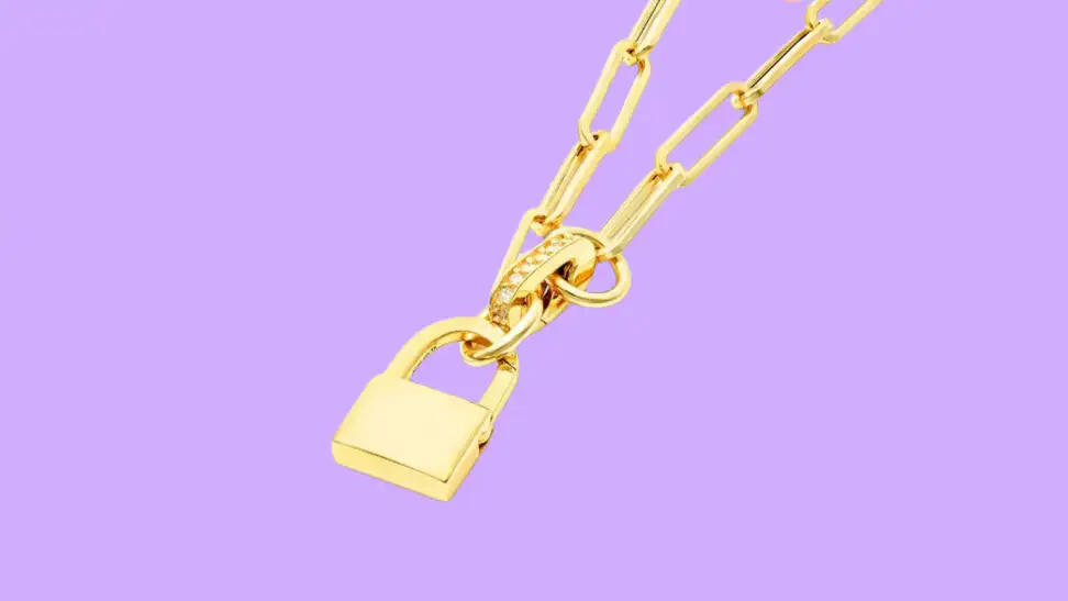 An image of a gold padlock charm on a gold paperclip chain necklace.