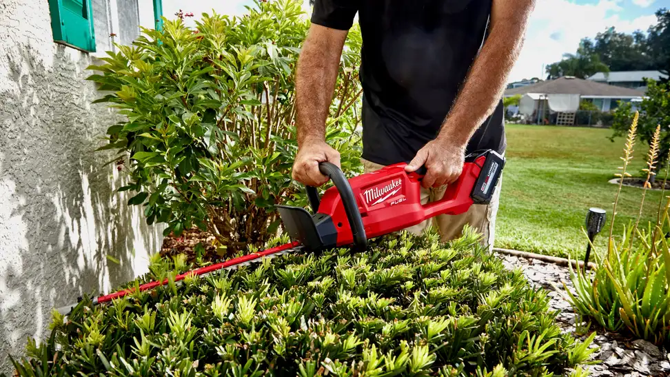 A red Milwaukee Tool hedge trimmer is being put to good use outdoors.