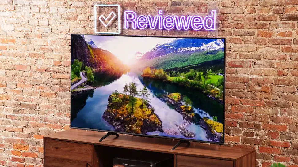The Hisense U6K displaying a colorful 4K image of a river and a sunset while it sits in front of a brick wall in a living room setting