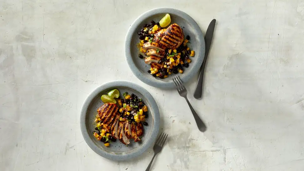 Two plates of grilled chicken on a gray countertop.
