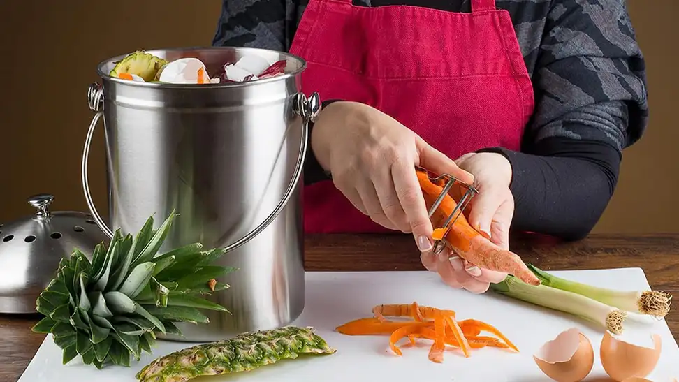 An Epica compost bin next to someone cutting up food in a kitchen.