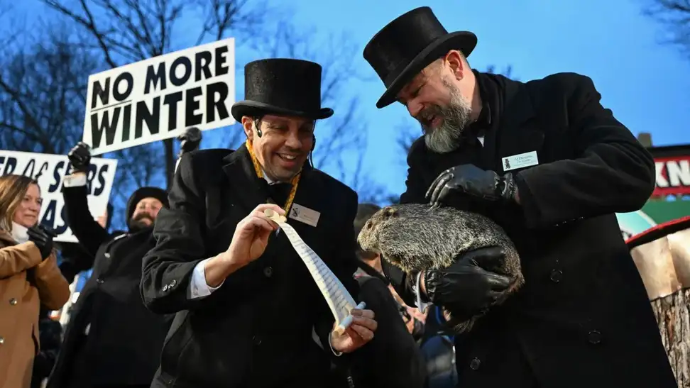 Man holds groundhog while "No More Winter" sign is held up in the background