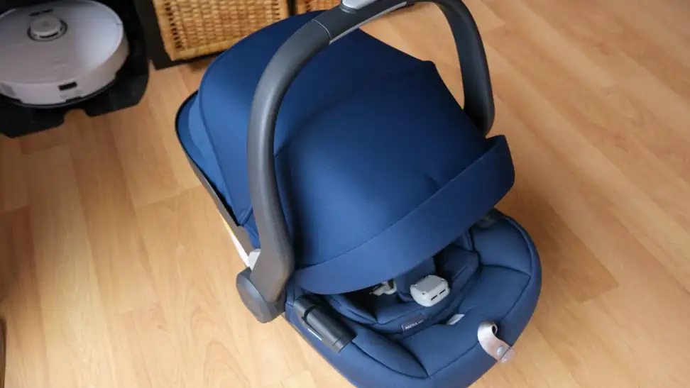 The Uppababy Mesa Max car seat in navy blue with hooded shade pulled all the way down on top of hardwood floor.