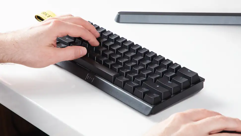 Close up angled shot of the Wooting 60he keyboard on a white desk with a hand on it