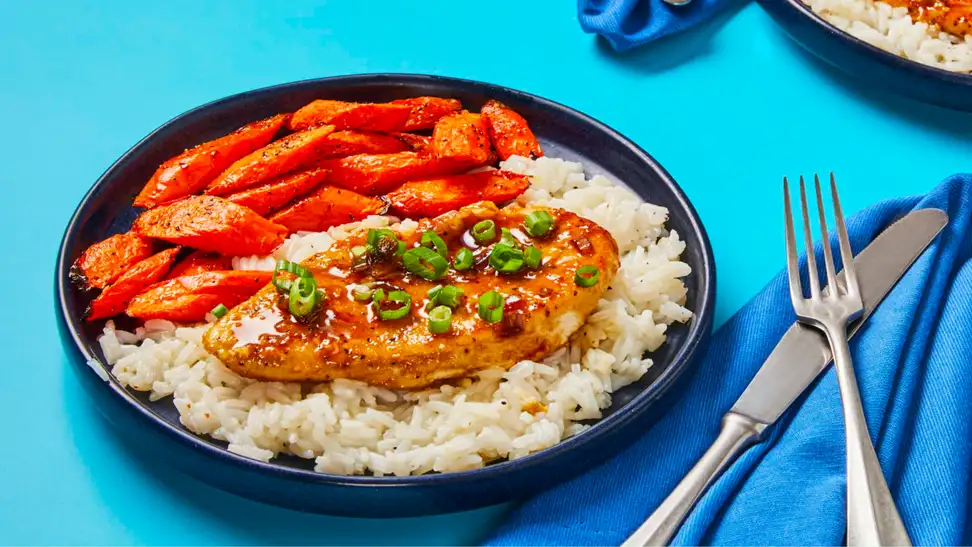 A plate of sweet and saucy garlic chicken next to utensils and a blue napkin.