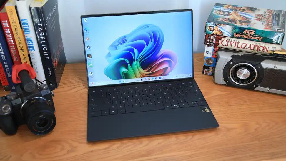 The 2024 Dell XPS 13 9345 laptop sitting on a desk next to a camera and several books.
