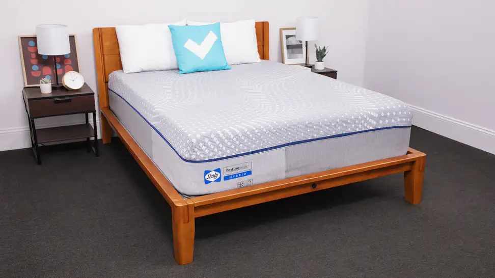 The Sealy Posturepedic mattress inside of a wooden frame with two pillows on top indoors.