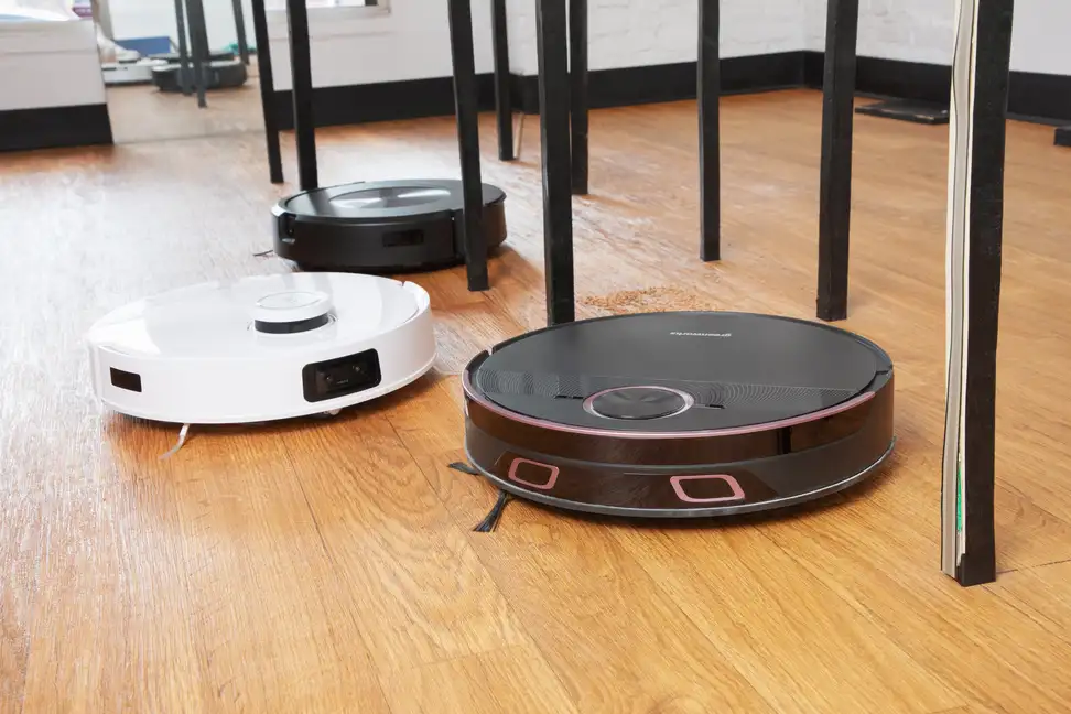 Three robot vacuums on a wood floor dodge table legs