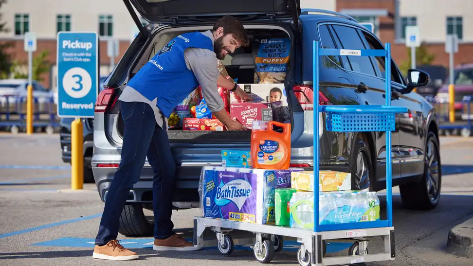 A Sam’s Club employee loads a customer’s SUV with bulk groceries and household essentials during a curbside pickup at a designated parking spot.
