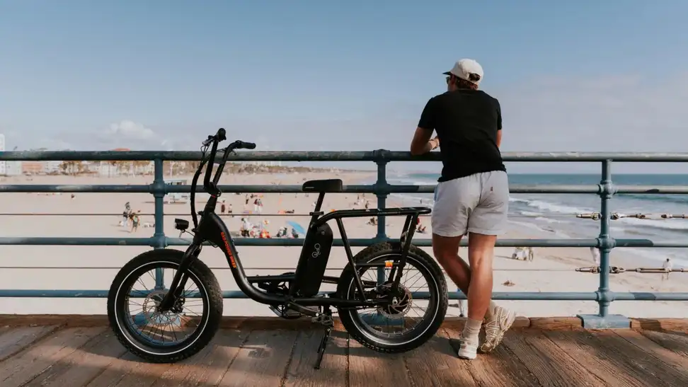 Man stands next to e-bike on California pier overlooking the beach