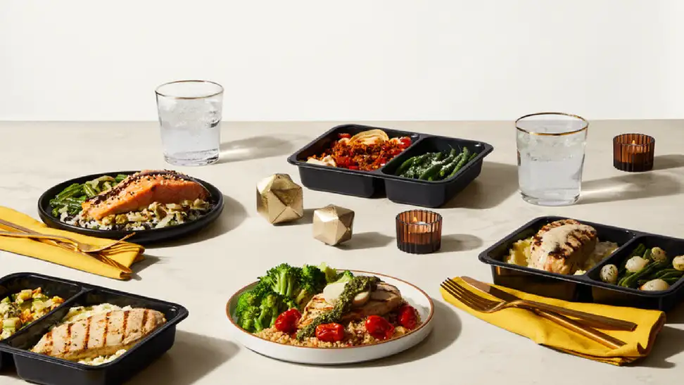 Multiple meals with seared chicken, salmon, vegetables on a beige table with geometric gold objects interspersed