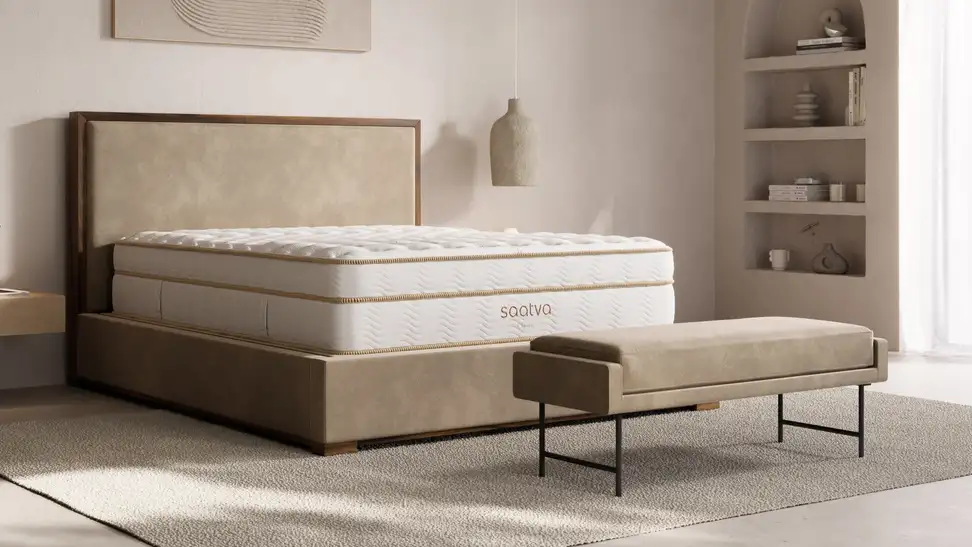 A modern bedroom featuring a white Saatva Classic mattress on a low-profile upholstered bed frame with warm wood accents, styled with neutral decor and soft natural lighting—an image highlighting the Saatva Memorial Day sale on luxury mattresses.
