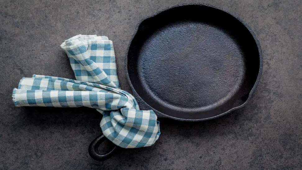Dirty cast iron with blue and white checkered towel tied to the handle