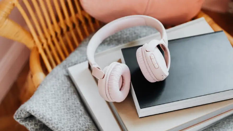 A pair of pink over-the-ear headphones sits on a stack of books