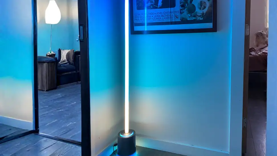Tall LED floor lamp casting blue ambient light in a modern hallway, with illuminated base and vertical light tube creating colorful mood lighting.
