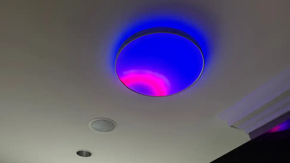 Smart ceiling fixture illuminating a room with vivid blue and magenta lighting, demonstrating customizable RGB ambient effects and ceiling wash lighting.