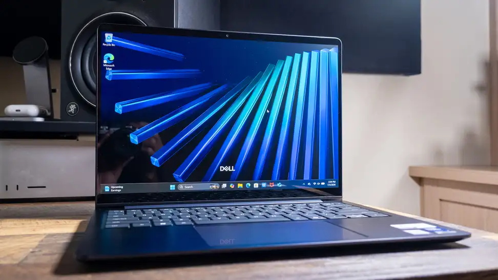 Dell 14S (DS14260) laptop open and turned on, sitting on a wooden surface. Blue abstract image displayed on screen.