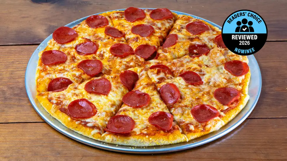 A pepperoni pizza sits on a pizza pan on a wooden table