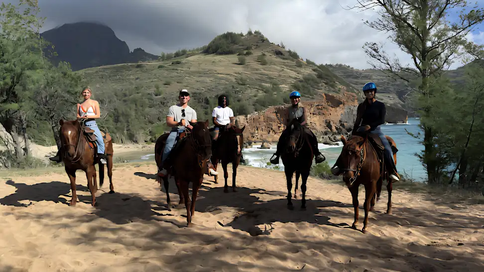 Group of people riding horses along a scenic beach trail with ocean cliffs in the background.