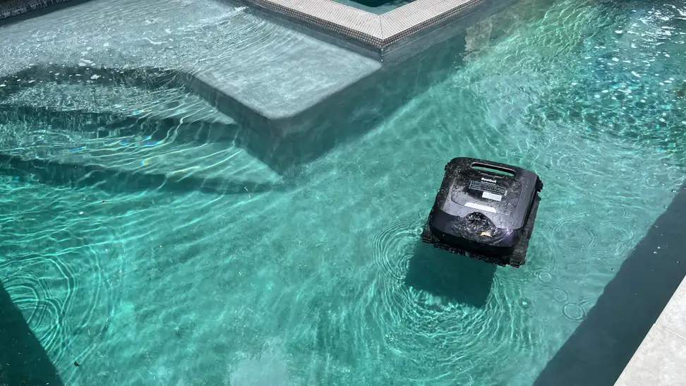 Black Beatbot Aquasense X Robot Pool Cleaner shown cleaning a pool with steps on the left.