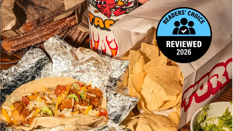 A spread of Torchy's Tacos food including a stuffed taco, tortilla chips, churros, and a branded drink cup, overlaid with a Readers' Choice Reviewed 2026 badge.